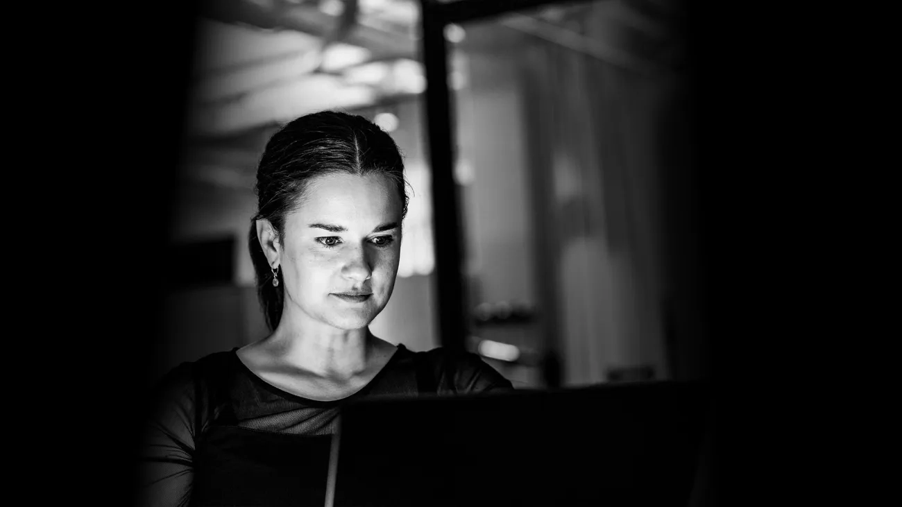 Focused woman working on a laptop in dim lighting.