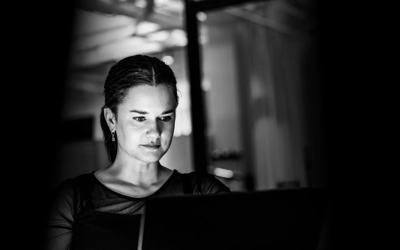 Focused woman working on a laptop in dim lighting.