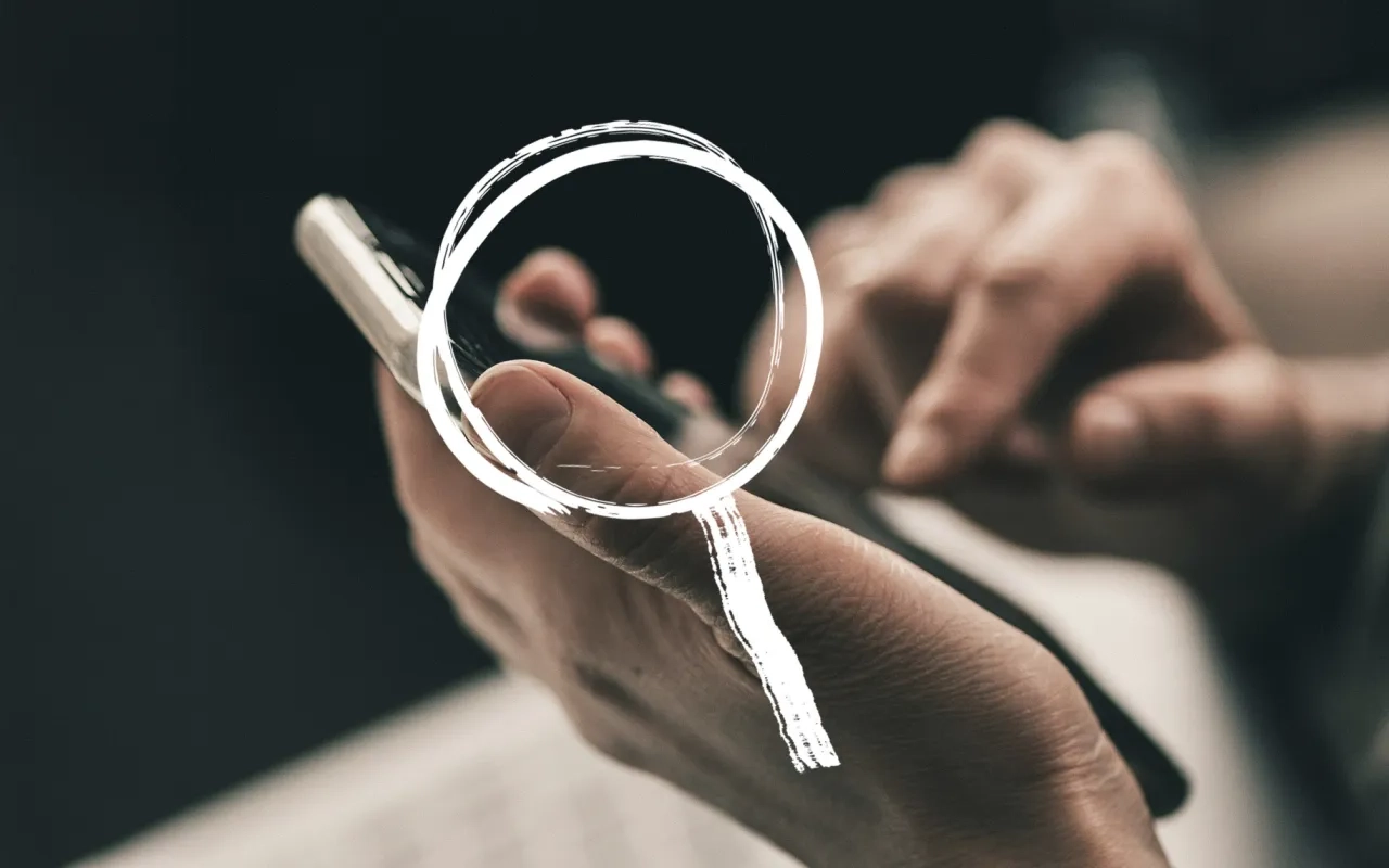 Hands holding a smartphone, magnifying glass drawn over screen.
