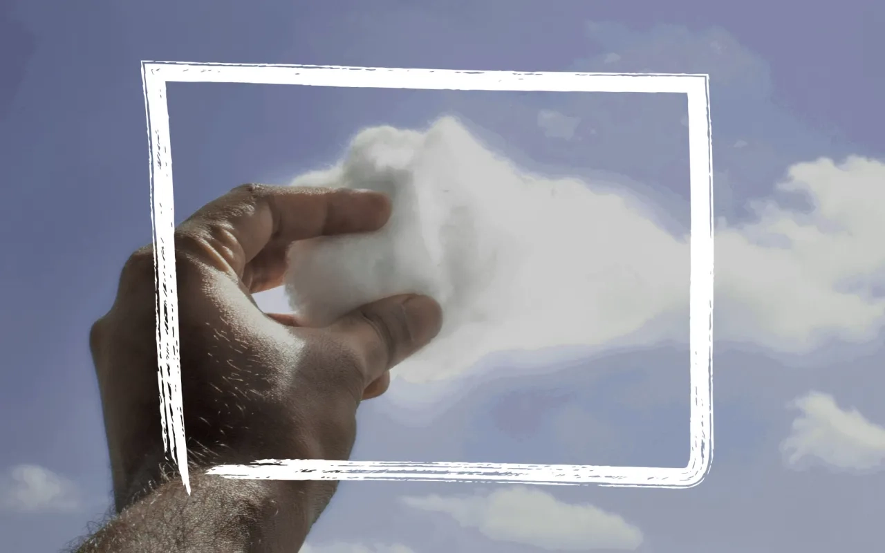 Hand holding fluffy cloud against a blue sky with scattered clouds.