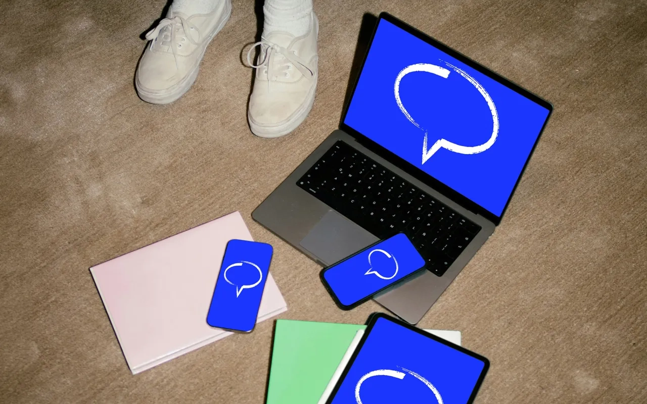 Laptop, tablet, and phones with blue chat bubble icons on carpet.