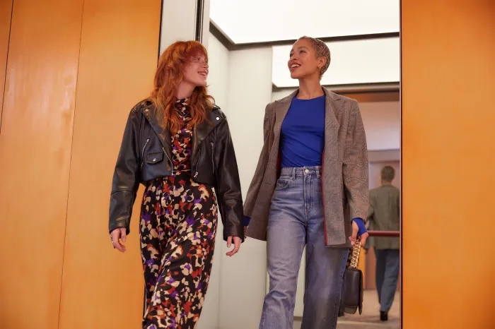 Two people walking in a hallway, smiling at each other, one holding a briefcase.